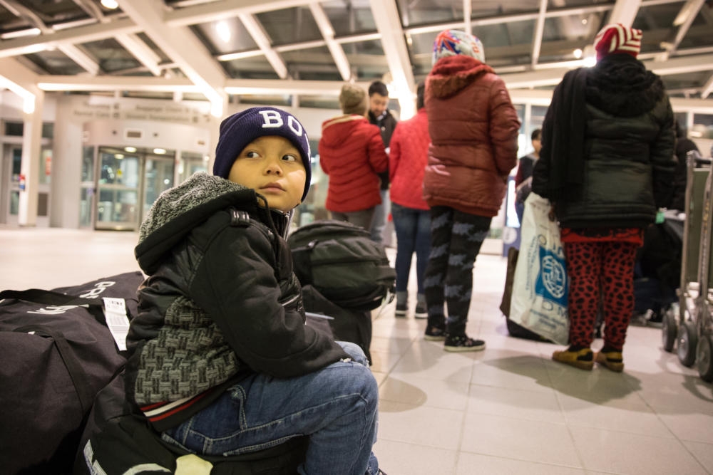 A young refugee boy sits on his family's baggage in the Manchester–Boston Regional Airport shortly after arriving with his mom and his sister. His mother fled Bhutan as a refugee in the early '90s, and lived in a refugee camp in Nepal until recently resettling in Manchester, New Hampshire. (Ryan Caron King for NENC)